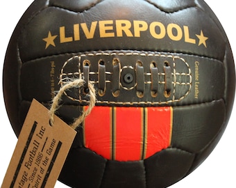 May include: A brown leather football with the word "LIVERPOOL" in gold lettering and a star on each side. The ball has a red and gold stripe and a tag that reads "Vintage Football Inc Since 1886 The Spirit of the Game".