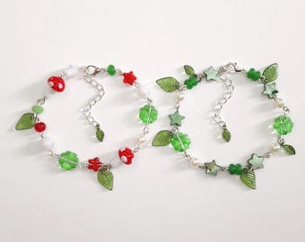 May include: Two delicate bracelets with silver chains, adorned with red and white mushroom beads, green leaf charms, and star-shaped beads. The bracelets also feature clear green flower-shaped beads and small white beads.