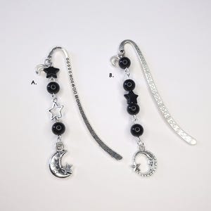 Puede incluir: Dos marcadores de metal plateado con dijes celestiales. Un marcador presenta un dije de luna creciente y estrella, cuentas negras y dijes de estrella. El otro tiene un dije de luna creciente y estrella, cuentas negras y dijes de estrella.