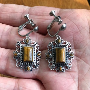 May include: A pair of silver clip-on earrings with a rectangular tiger's eye stone set in a filigree design.