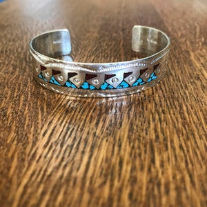 May include: Silver bracelet with turquoise and red inlay. The bracelet has a geometric pattern.
