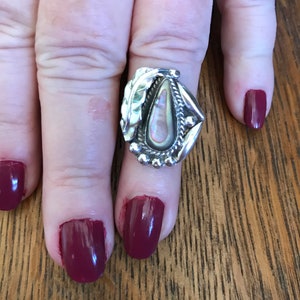 May include: A silver ring with a pearlescent abalone shell stone set in a leaf design. The ring is on a finger with burgundy nail polish.