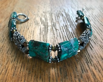 May include: A turquoise and silver bracelet with square-shaped turquoise stones and silver accents. The bracelet has a clasp closure.