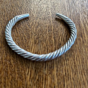 May include: A silver twisted bangle bracelet. The bracelet is made of a thick, twisted wire and has a smooth, polished finish.