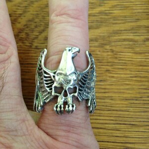 May include: A silver ring featuring a detailed eagle skull design with spread wings.
