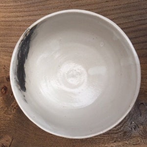 May include: A white ceramic bowl with a black brushstroke design. The bowl is round and has a smooth, glossy finish.