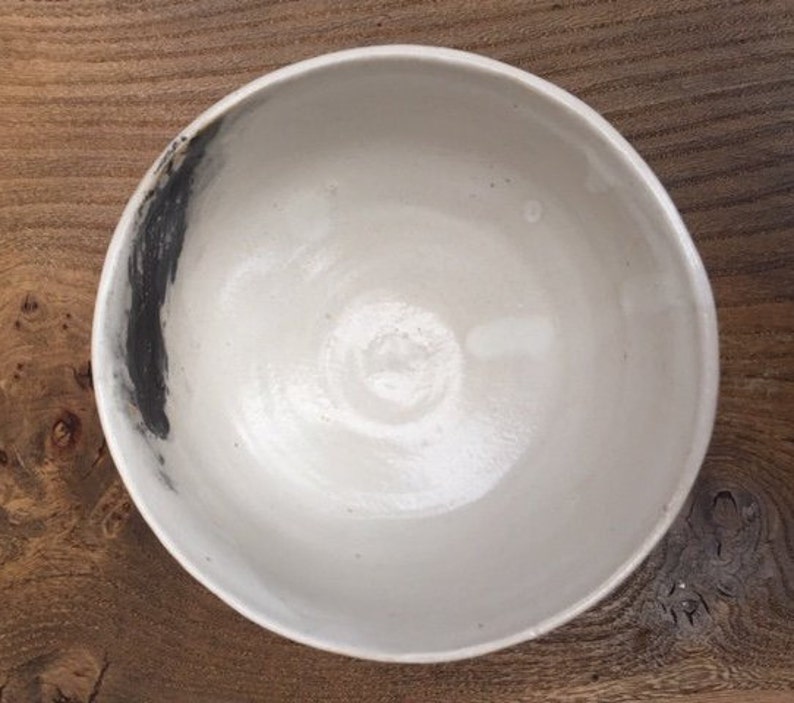 May include: A white ceramic bowl with a black brushstroke design. The bowl is round and has a smooth, glossy finish.