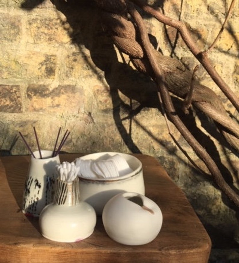 May include: Three white ceramic containers with a rustic, natural look. The containers are different sizes and shapes, with one featuring a black and white pattern. The containers are sitting on a wooden surface.