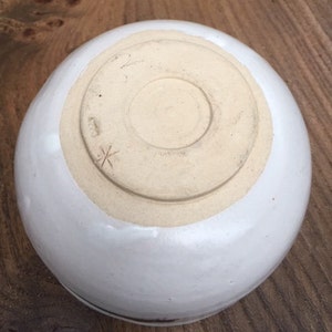 May include: White ceramic bowl with a brown rim. The bottom of the bowl has a small cross mark.