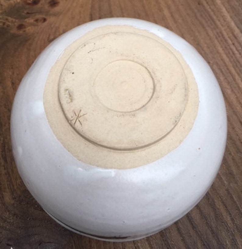 May include: White ceramic bowl with a brown rim. The bottom of the bowl has a small cross mark.
