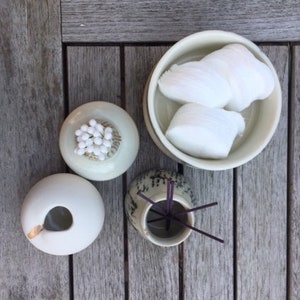 May include: Three ceramic bowls on a wooden surface. One bowl contains white cotton balls, another contains white cotton candy, and the third bowl contains incense sticks.