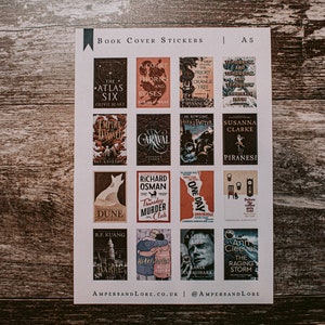 May include: A sheet of A5 book cover stickers featuring popular book covers. The stickers include titles like "The Atlas Six", "A Court of Thorns and Roses", "The Priory of the Orange Tree", "Empire of the Vampire", "Caraval", "Harry Potter", "Piranesi", "Dune", "Thursday Murder Club", "One Day", "The Raging Storm", and "Heartstopper".