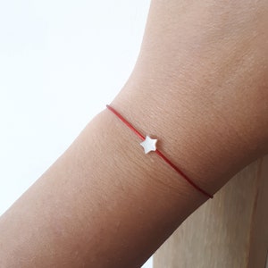 Puede incluir: Un brazalete de cuerda roja con un pequeño dije de estrella blanca.