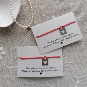 Può includere: Due braccialetti di corda rossa con ciondoli a forma di cuore in argento. Ogni braccialetto è accompagnato da un biglietto bianco con il testo "True friends are never apart, Maybe in distance but never in heart."