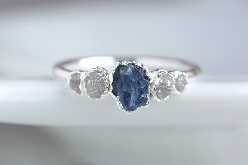 May include: A silver ring with a blue sapphire and four white diamonds. The ring is set in a simple band and the stones are all rough cut.