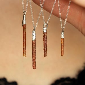 May include: Four necklaces with silver chains and pendants. Each pendant is a brown, textured crystal with silver caps. The crystals vary in size and shape, with a natural, organic appearance. The necklaces are displayed against a blurred background.