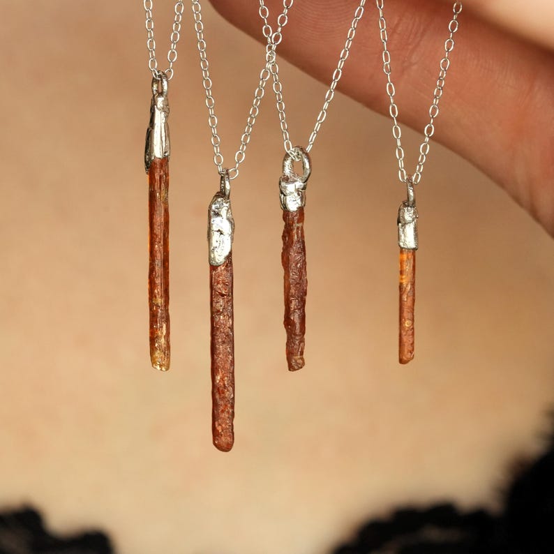 May include: Four necklaces with silver chains and pendants. Each pendant is a brown, textured crystal with silver caps. The crystals vary in size and shape, with a natural, organic appearance. The necklaces are displayed against a blurred background.