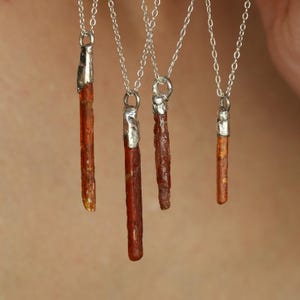 May include: Close-up of several necklaces with silver chains and pendants. Each pendant is a slender, reddish-brown mineral with a silver cap. The necklaces are displayed against a neutral background, highlighting the natural beauty of the gemstones.