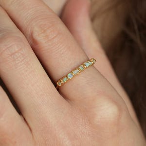 Op de afbeelding: Een gouden ring met een rij kleine, ovale opalen. De opalen hebben een melkachtige witte en iriserende kleur. De ring is gezet in een getextureerde gouden band.