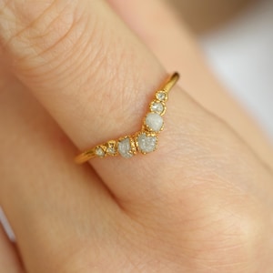 Könnte beinhalten: Ein goldener Ring mit einer geschwungenen Reihe kleiner, weißer, roher Diamanten.