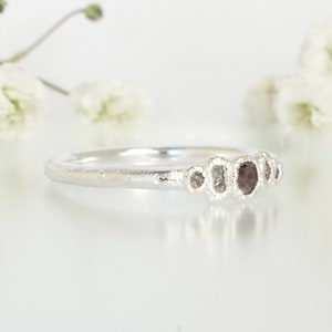 May include: A silver ring featuring a row of five small, irregularly shaped diamonds. The diamonds are set in a textured band.