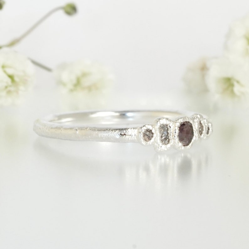 May include: A silver ring featuring a row of five small, irregularly shaped diamonds. The diamonds are set in a textured band.