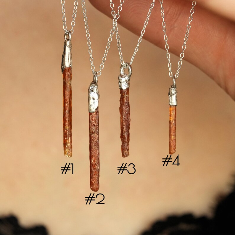 May include: Four silver chain necklaces with raw, brown-orange crystal pendants. Each crystal is unique in shape and size, with silver caps at the top. The necklaces are numbered #1 through #4.