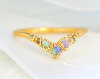 Puede incluir: Un anillo de banda de oro con una fila de piedras preciosas de ópalo iridiscente en forma de V.