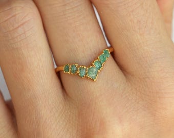 Puede incluir: Anillo de oro con una fila de piedras preciosas verdes en forma de V.