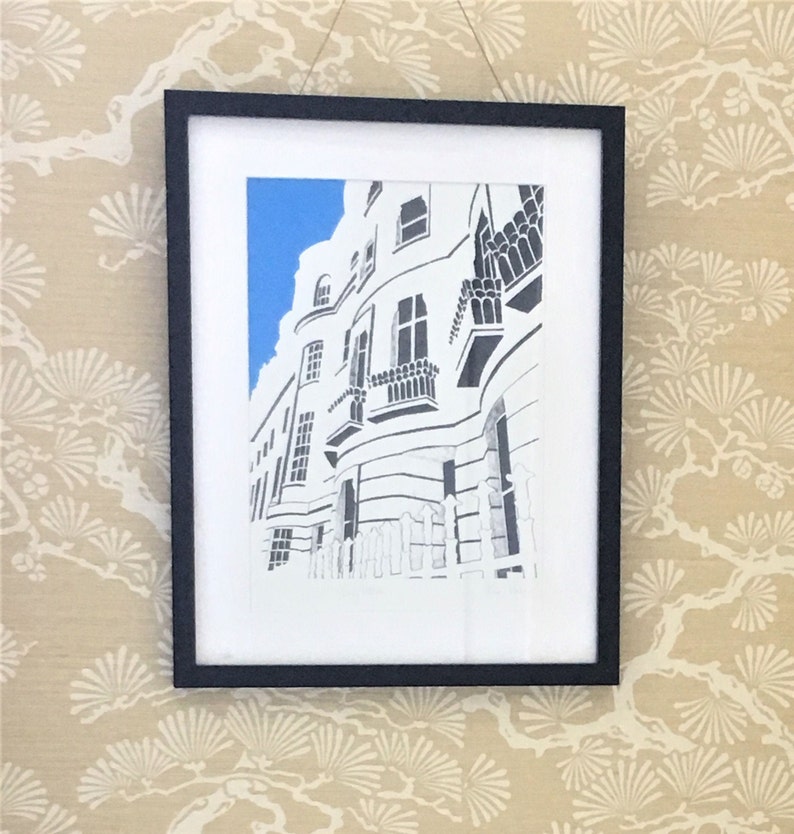 May include: A black and white drawing of a white building with a blue sky in the background. The building has many windows and a balcony. The drawing is framed in a black frame.