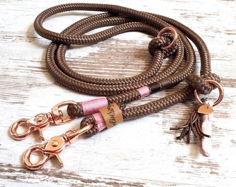 May include: A brown rope dog leash with two rose gold clips and a pink and brown tassel. The leash has a brown leather tag with the text "Clixstyle" on it.