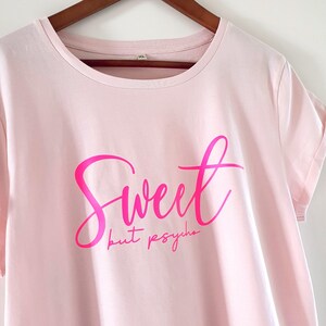 Może przedstawiać: R&oacute;żowa koszulka z r&oacute;żowym i białym nadrukiem z napisem "Sweet but psycho".