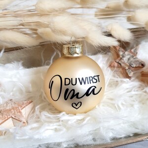 May include: Gold Christmas ornament with the text "DU WIRST OMA" in black lettering and a small heart.