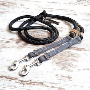May include: A black rope dog leash with two gray leather leashes attached. The leashes have silver clips and a brown leather accent.