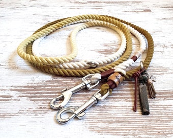 May include: A green, white, and brown rope dog leash with two silver clips and a brown leather accent. The leash has a green tassel and a silver charm.