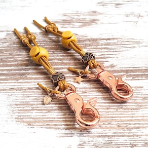 May include: Two gold-toned dog leash clips with yellow and brown rope accents. Each clip has a small charm attached, one with a star and the other with a heart.