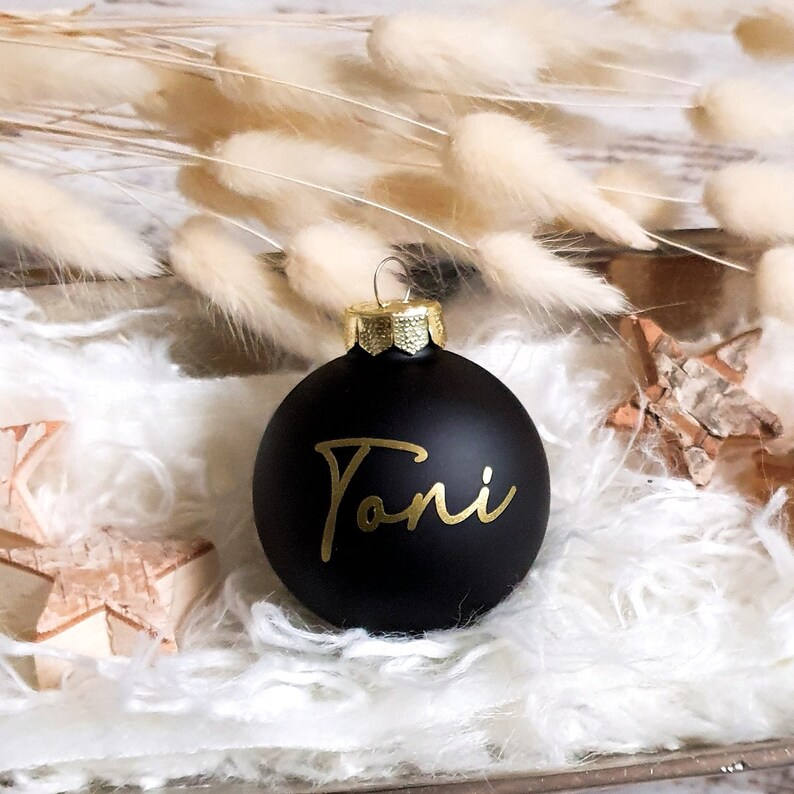 May include: A black Christmas ornament with the name "Toni" written in gold script.