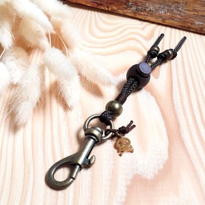 May include: A brown leather keychain with a gold charm and a black cord. The cord has a wooden bead and a metal clasp.
