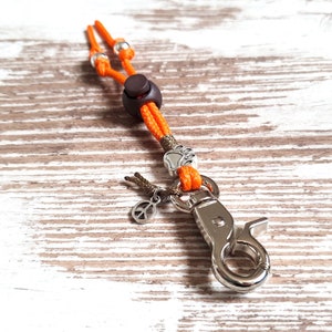 May include: Orange and brown rope keychain with a silver clip, a peace sign charm, and a paw print charm.