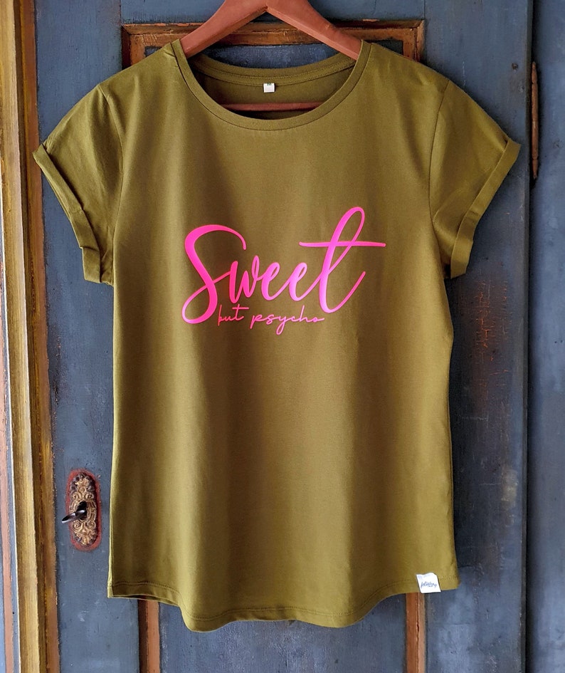 Może przedstawiać: Zielona koszulka z napisem "Sweet but psycho" w r&oacute;żowych literach.
