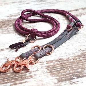 May include: A double dog leash with a burgundy rope leash and a gray leather leash with rose gold hardware. The rope leash has a star charm.