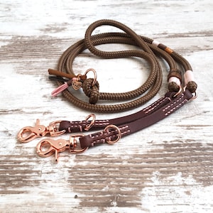 May include: A brown rope dog leash with two brown leather leashes attached. The leashes have pink stitching and rose gold metal clips.