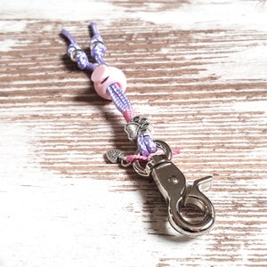 May include: A purple and pink rope dog leash with a silver clip, a pink heart charm, and a silver paw print charm.