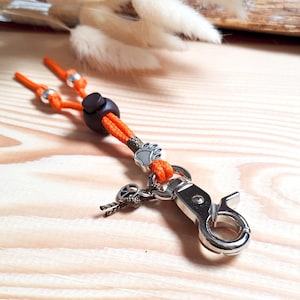 May include: Orange and brown key chain with a silver paw print charm and a silver clasp. The key chain has a brown bead and a silver bead.