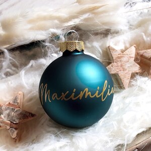May include: Teal blue Christmas ornament with the name Maximilian written in gold lettering.