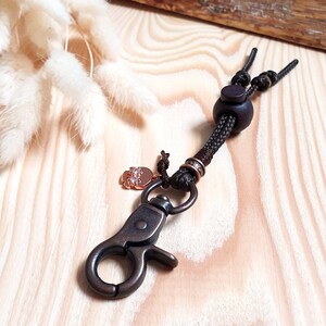 May include: A brown leather keychain with a metal clasp and a small charm with rhinestones. The keychain has a brown wooden bead and a brown cord.