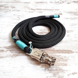 Op de afbeelding: Zwarte touwhalster voor honden met een turquoise en zwart gevlochten accent en een zilveren draaiklip.