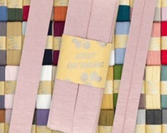 May include: A pack of 50 yards of light pink double fold bias tape. The tape is packaged on a yellow label with the words "Jersey Bias Binding" printed on it.