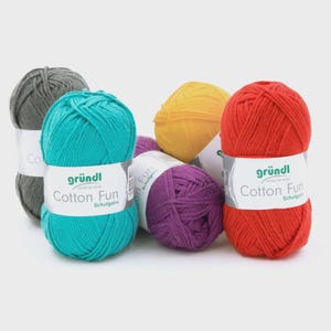 Puede incluir: Un conjunto de ovillos de lana coloridos en tonos turquesa, rojo, amarillo, morado y gris. Cada ovillo tiene una etiqueta blanca con el texto "Cotton Fun" y la marca "gründl". La lana es probablemente de algodón y adecuada para proyectos de punto o ganchillo.