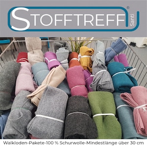 Könnte beinhalten: Ein Einkaufswagen aus Metalldraht gefüllt mit Rollen aus verschiedenen farbigen Filzen. Die Filze sind alle aus 100% Wolle und mindestens 30 cm lang. Der Wagen ist mit "Stofftreff Santi" beschriftet.
